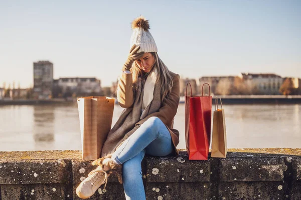 Woman in warm clothing with shopping bags is worried because she spent too much money. Toned image.