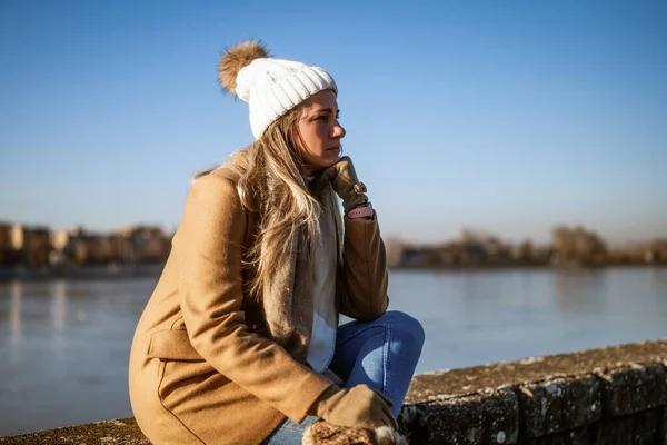 Smutna Kobieta Ciepłym Ubraniu Siedząca Nad Rzeką Słoneczny Zimowy Dzień — Zdjęcie stockowe