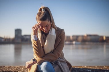 Nehir kenarında otururken baş ağrısı çeken endişeli bir kadın. Tonu ayarlanmış resim.