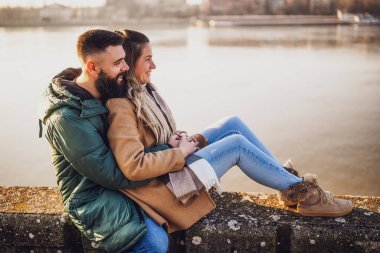 Mutlu çift kucaklaşırken nehrin kenarında oturmanın keyfini çıkarın..