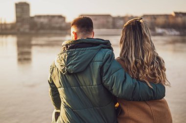 Mutlu çift kucaklaşırken nehrin kenarında oturmanın keyfini çıkarın..