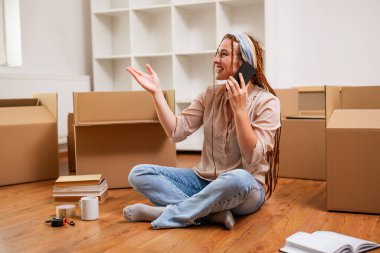 Yeni dairesine taşınırken saçı örgülü, telefonda konuşan modern kızıl kadın..