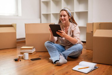 Yeni daireye taşınırken dijital tablet kullanan örgülü modern kızıl kadın..