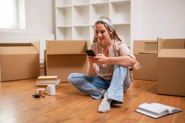 Yeni dairesine taşınırken saçı örgülü, modern kızıl bir kadın telefon kullanıyor..