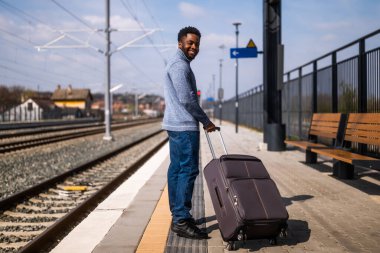 Tren istasyonunda duran bavullu mutlu adam..