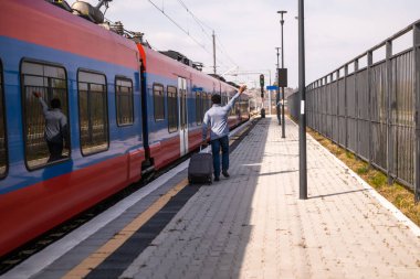 Trenden ayrılan bir adama el sallıyor ve tren istasyonunda bavuluyla koşuyor..