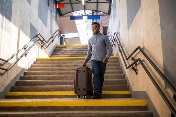 Happy man with suitcase walking down a stairs in railway station.