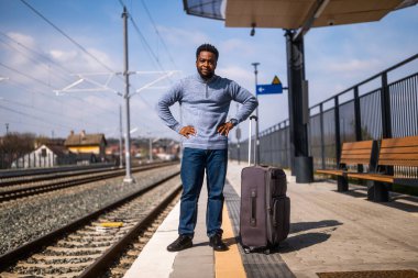 Tren istasyonunda duran bavullu endişeli bir adam..