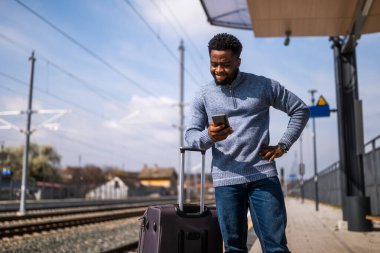 Elinde bavul ve cep telefonu olan kızgın bir adam tren istasyonunda bekliyor..
