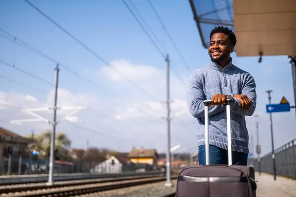 鉄道駅に立っているスーツケースを持つ幸せな男 ロイヤリティフリーのストック写真