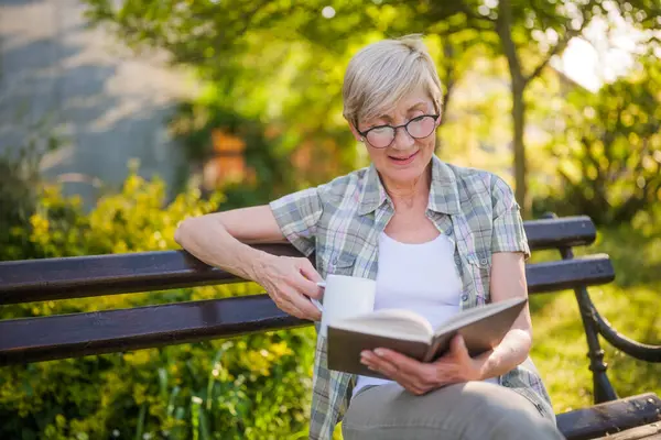 Feliz Mujer Mayor Disfruta Leyendo Libro Tomando Café Banco Jardín Imagen de archivo