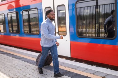 Tren istasyonunda elinde bavulla koşan bir adam var..