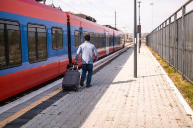 Tren istasyonunda elinde bavulla koşan bir adam var..