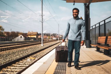 Bavullu mutlu adam tren istasyonunda yürüyor..