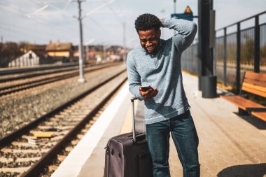 Tren istasyonunda duran bavulu ve cep telefonu olan endişeli bir adam..