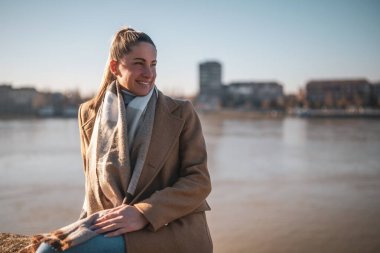 Sıcak giysili güzel bir kadın güneşli bir kış gününde nehir kenarında dinlenmekten hoşlanır. Tonu ayarlanmış resim.