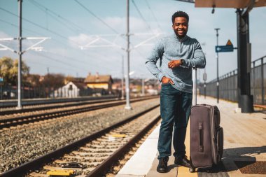 Tren istasyonunda duran bavullu mutlu adam..