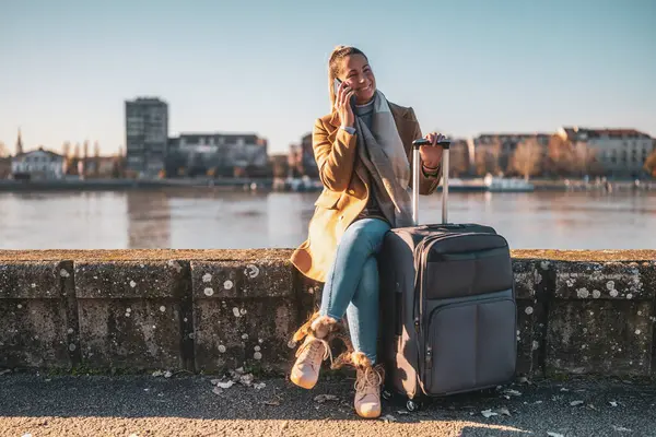 Bavullu mutlu bir turist nehir kenarında dinlenirken telefonla konuşuyor. Tonu ayarlanmış resim.