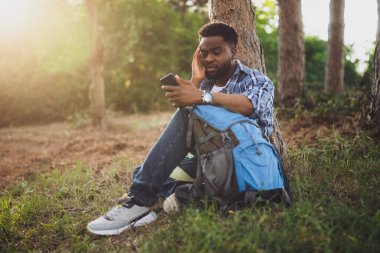 Endişeli yürüyüşçü kayboldu ve doğada otururken doğru yönü bulmak için bir telefon kullanıyor..