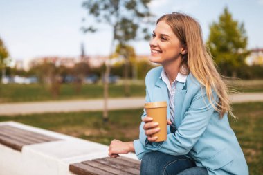 Güzel bir iş kadını bankta otururken kahve içiyor..