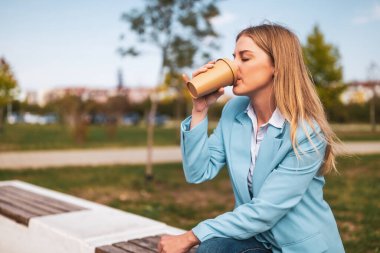 Güzel bir iş kadını bankta otururken kahve içiyor..