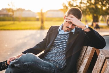 Güneş batarken parktaki bankta oturan gözlüklü üzgün iş adamı.