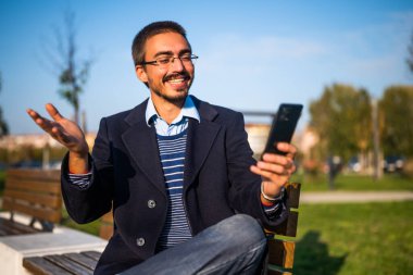 Güneşli bir sonbahar gününde parktaki bankta otururken gözlüklü mutlu bir işadamı cep telefonu kullanıyor..