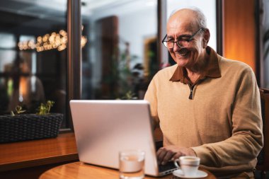 Gözlüklü, dizüstü bilgisayarı olan ve akşam kafede oturup kahve içen mutlu bir son sınıf öğrencisi..