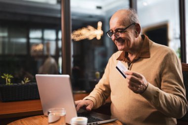 Akşamları kafede otururken kredi kartı ve dizüstü bilgisayar kullanarak gözlüklü neşeli bir son sınıf öğrencisi..