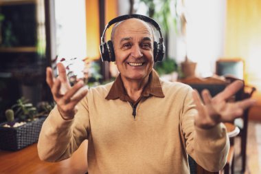 Gündelik giysiler içinde, kablosuz kulaklıklı neşeli bir adamın portresi. Kameraya bakıyor ve şehirdeki kafede otururken bilgisayarından bir video görüşmesi sırasında konuşuyor..