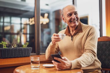 Keyifli son sınıf öğrencisi rahat bir kafede dinlenirken cep telefonu kullanıyor ve kahve içiyor..