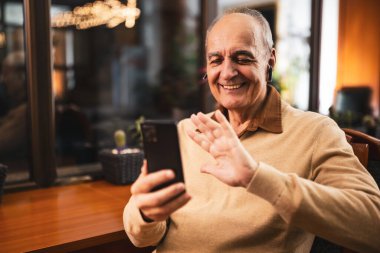 Neşeli son sınıf öğrencisi cep telefonu ve kulaklık kullanırken el sallıyor. Şehir barında rahatlıyor ve teknolojiyi kullanıyor..