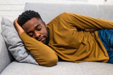 Yorgun Afro-Amerikalı adam rahat evinde kanepede uyumaktan zevk alıyor..