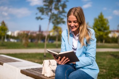 Şık bir iş kadını şehirde işe ara veriyor, bankta oturuyor ve açık havada kitap okuyor..