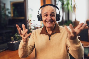  Kafedeki video görüşmesi sırasında gülümseyen ve el kol hareketi yapan kulaklıklı mutlu emekli adam..