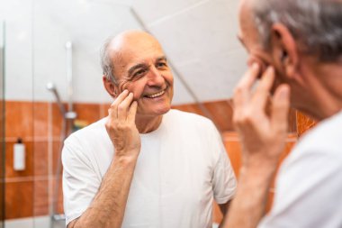 Banyodaki aynada beyaz saçlı gülümseyen ve tenine dokunan son sınıf öğrencisinin portresi..