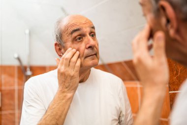 Banyodaki aynanın önünde duran ve göz torbalarına bakan kıdemli adam memnun değil.. 