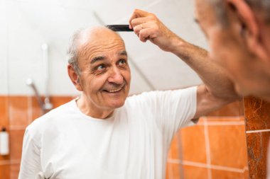 Banyoda aynada kendine bakarken gri saçlarını tarayan mutlu son sınıf öğrencisinin portresi..