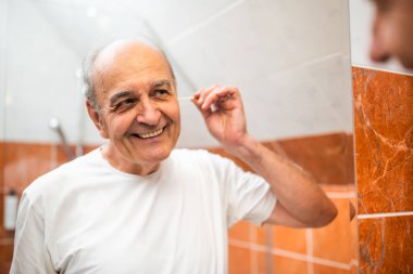 Banyoda aynanın önünde dikilirken kulak temizliği için pamuk çubuğu kullanan mutlu yaşlı adamın portresi..