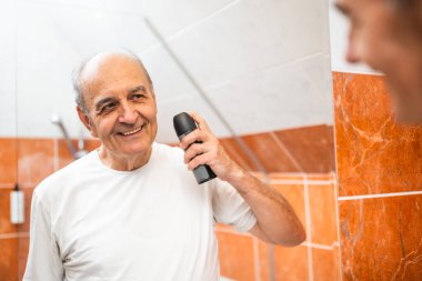 Kendinden emin, kendinden emin bir adamın portresi. Kokulu vücut spreyi kullanırken banyo aynasında yansımasına bakıyor..