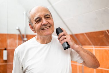 Deodorant kullanırken banyo aynasına bakan mutlu yaşlı adam, erkeksi bakımı, tazeliği ve kişisel hijyeni temsil ediyor..
