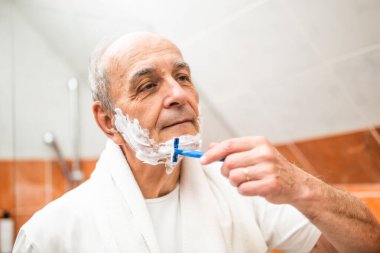 Banyodaki aynada kendine bakarken sakalını tıraş ederken tıraş bıçağı kullanan yaşlı adamın portresi..