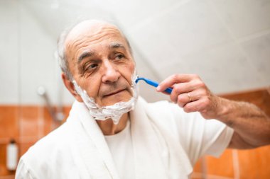 Son sınıf öğrencisi, sabah temizliği sırasında banyo aynasının önünde tıraş olurken sakalını jiletle tıraş ediyor..