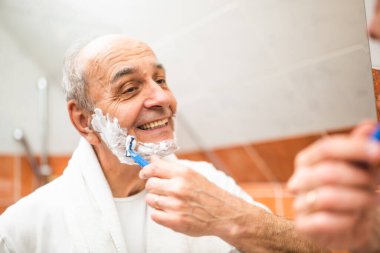 Gülümseyen son sınıf öğrencisinin sabah hijyen rutini sırasında banyo aynasının önünde tıraş olurken sakalını tıraş edişinin portresi. Günlük bakım ritüelini özenle yapıyor..