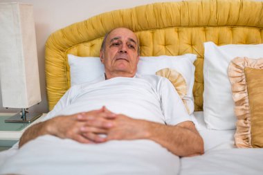 Pijamalı bunalımlı yaşlı adam yatakta tek başına yatıyor. Sabahın erken saatlerinde yaşlanma, endişe ve zihinsel sağlığın getirdiği yalnızlık ve duygusal stresi yakalamak.