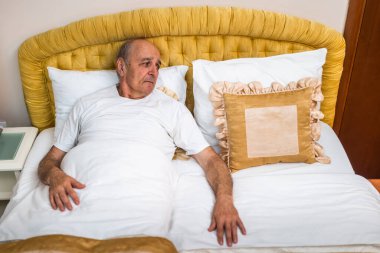 Yalnız, yaşlı bir adam yatakta tek başına uyanıyor, başka tarafa bakıyor ve üzüntüsünü ifade ediyor. Yaşlanmanın ve kederin derin derin duygusal tasviri.