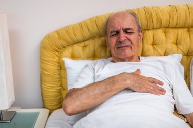 Endişeli son sınıf öğrencisi sabah uyanıp yatakta yattıktan sonra göğsünde ağrı hissediyor. Endişeli ve muhtemelen kalp krizi belirtileri gösteriyor..