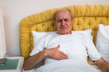 Evde yatağında yatarken karın ağrısından muzdarip son sınıf öğrencisi. İfadesi karın ağrısı ya da sindirim sorunlarından kaynaklanan rahatsızlığı yansıtıyor..