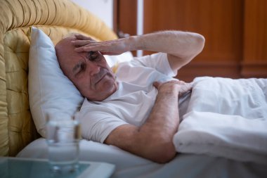 Bunalımlı son sınıf öğrencisi sabah erken saatlerde yatakta yatarken baş ağrısı çekiyor. Yaşlanma sürecinde zihinsel yorgunluk ve sağlık sorunları gösteriyor..