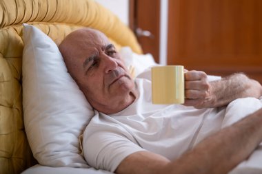 Endişeli son sınıf öğrencisi uyandıktan sonra yatakta kahve içiyor. Yorgunluk, endişe ve uykusuzluk belirtileri gösteriyor..